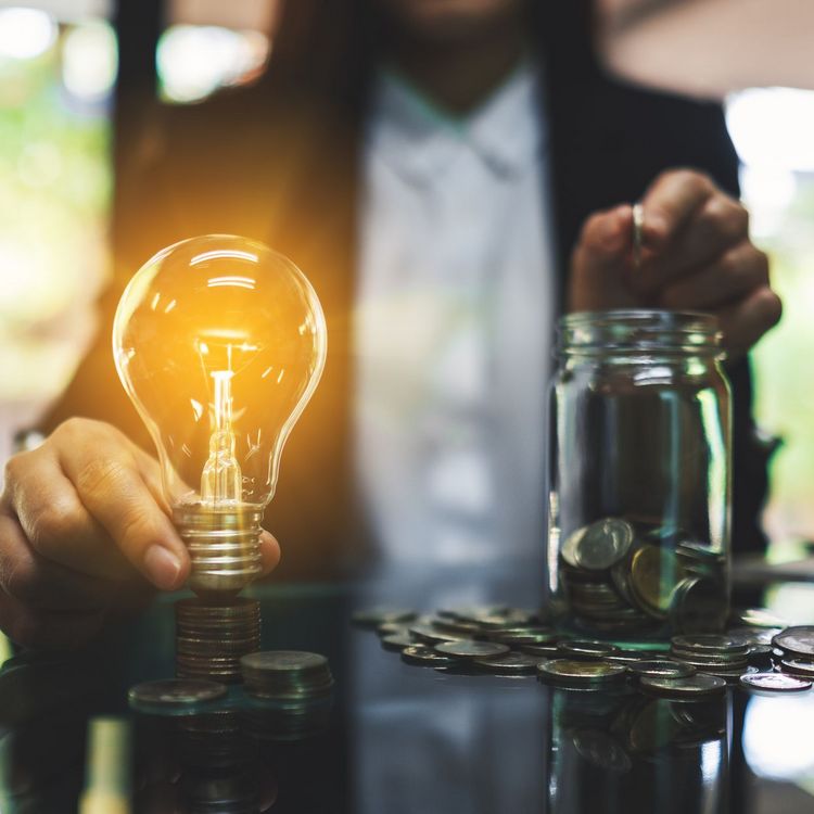 Businesswoman holding a light bulb over coins stack on the table